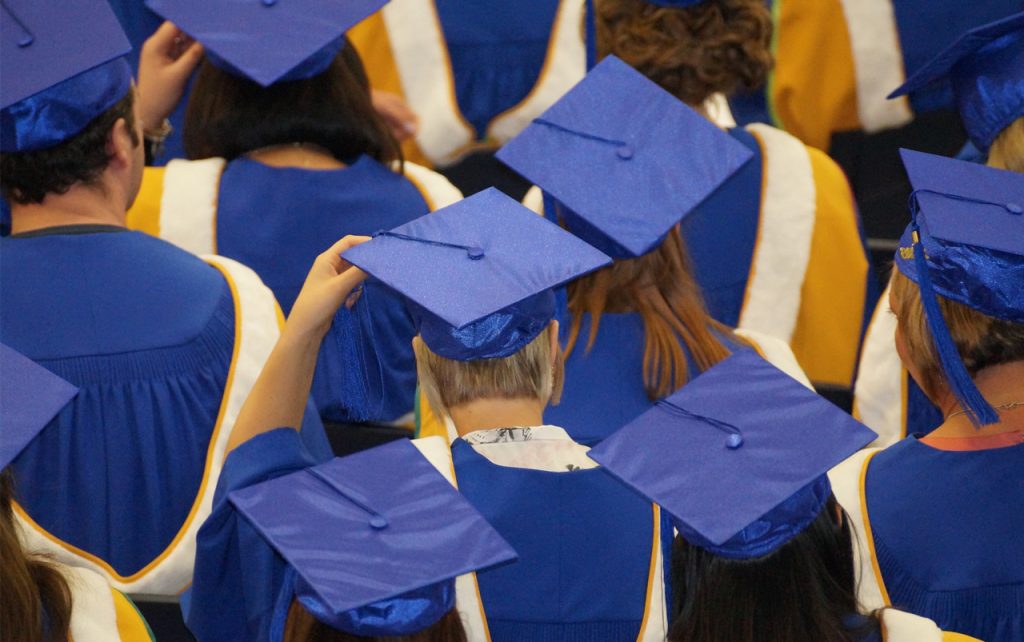Photo of students (from the back) at graduation wearing blue caps and gowns.