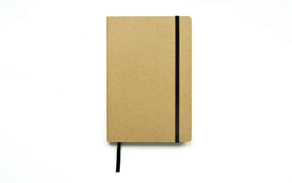 Illustration of a light brown journal notebook with a black placeholder and clasp on a white background.
