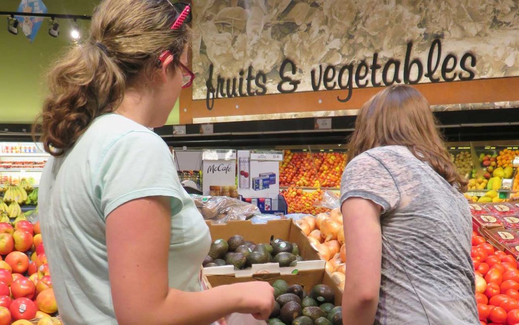 Two young females shopping in the produce section of a grocery store.