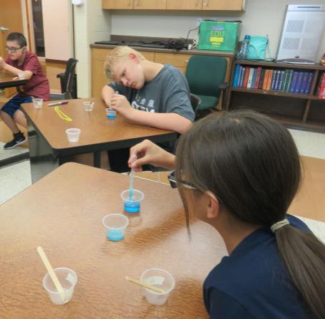 Three students sitting at tables and working on science experiments.