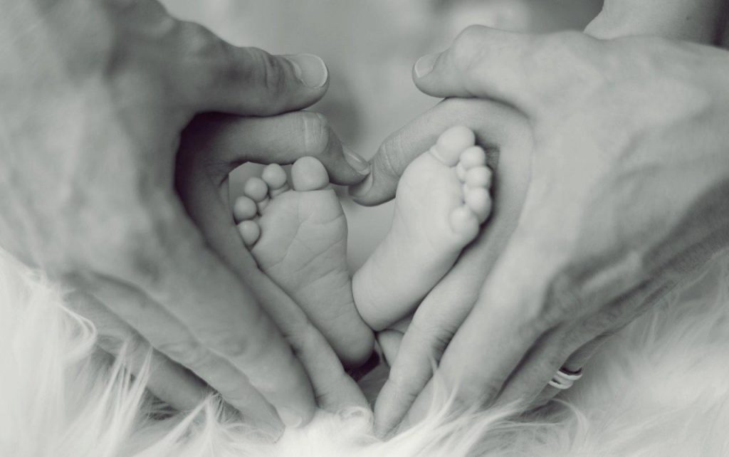 Family photo of baby's feet surrounded by mother and father's hands in the shape of a heart.