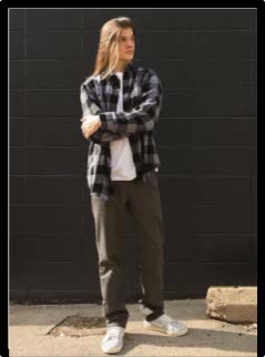 Jonah, a 2024 graduate, is wearing a black and gray plaid shirt while standing in front of a black brick wall for his Senior photo